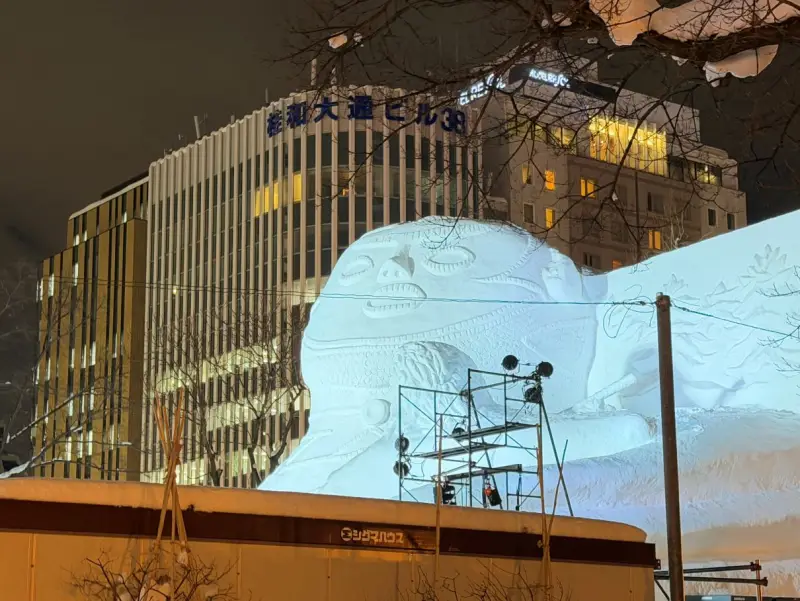 巨大な雪像。ビルの高さに迫る。照明のセッティング中で足場が残っている